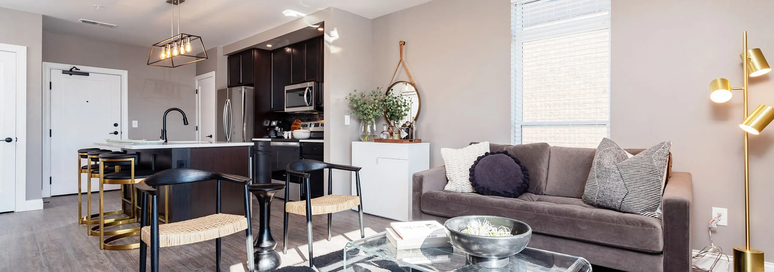 Bright and modern apartment living space featuring a sleek open-concept kitchen, cozy gray sofa, and elegant lighting accents.