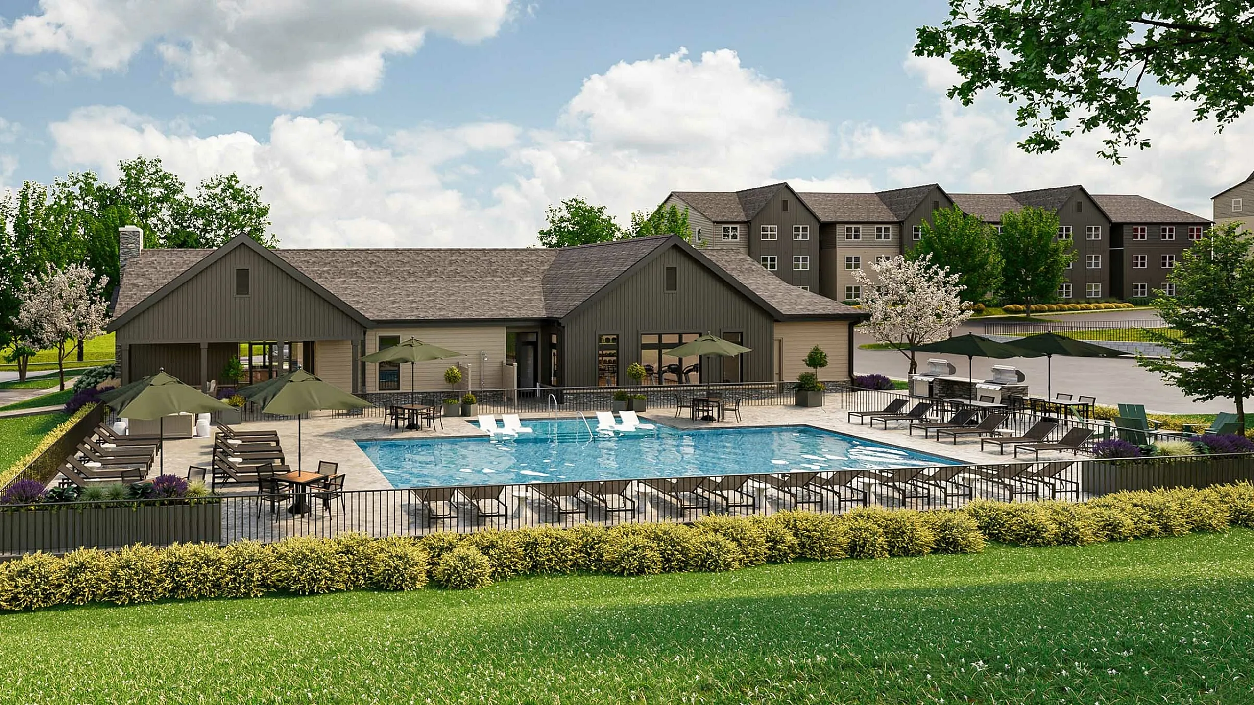 Charming apartment complex featuring a spacious outdoor pool area with sun loungers and shaded seating, surrounded by lush greenery and modern architecture.