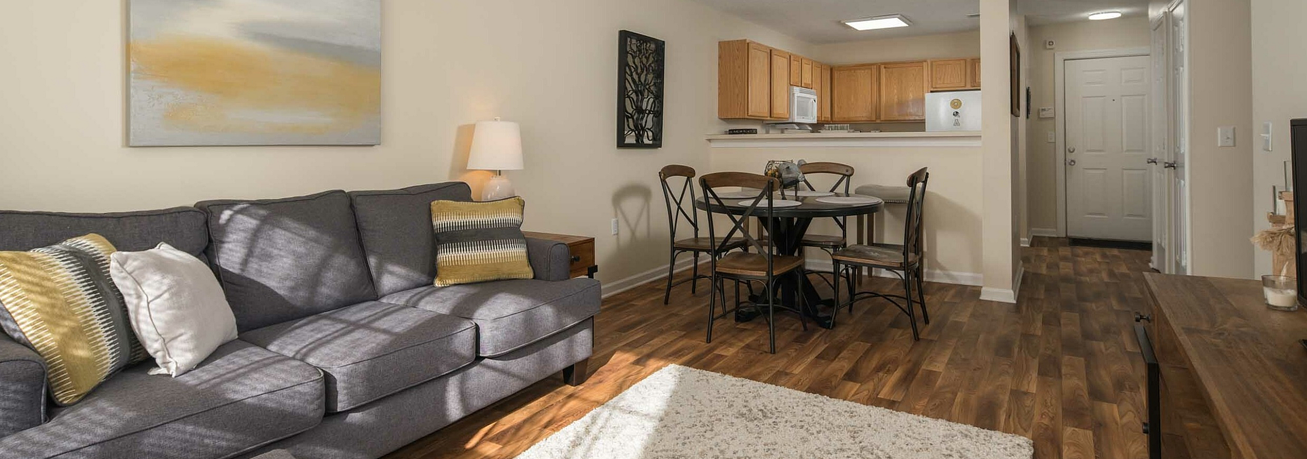 Bright and welcoming living area featuring a cozy gray sofa, stylish dining set, and open kitchen with warm wood cabinets.