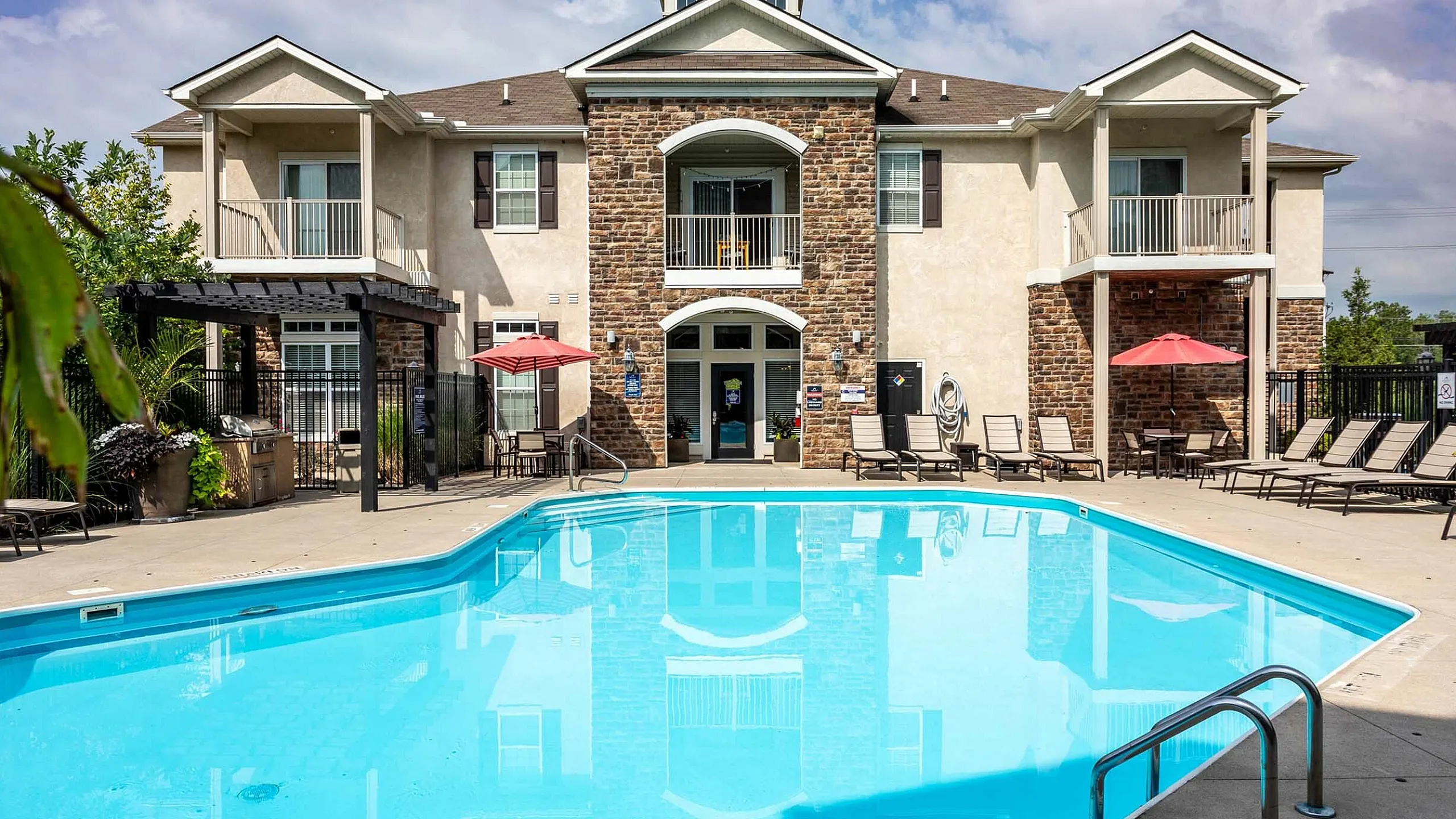 Elegant apartment complex with a sparkling blue pool, comfortable patio seating, and charming balconies.