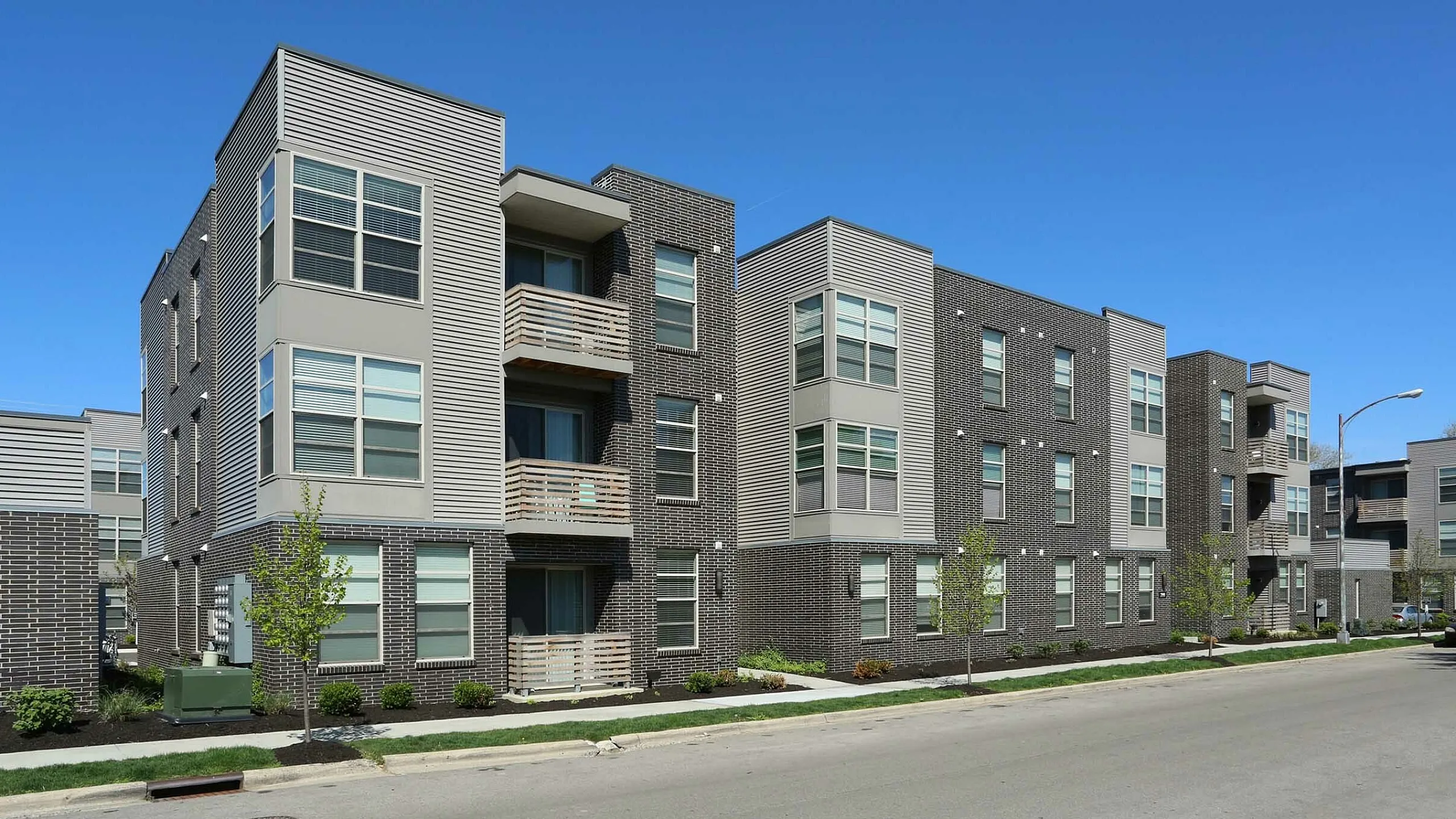 Modern apartment complex with sleek architecture, featuring expansive windows and stylish balconies against a clear blue sky.
