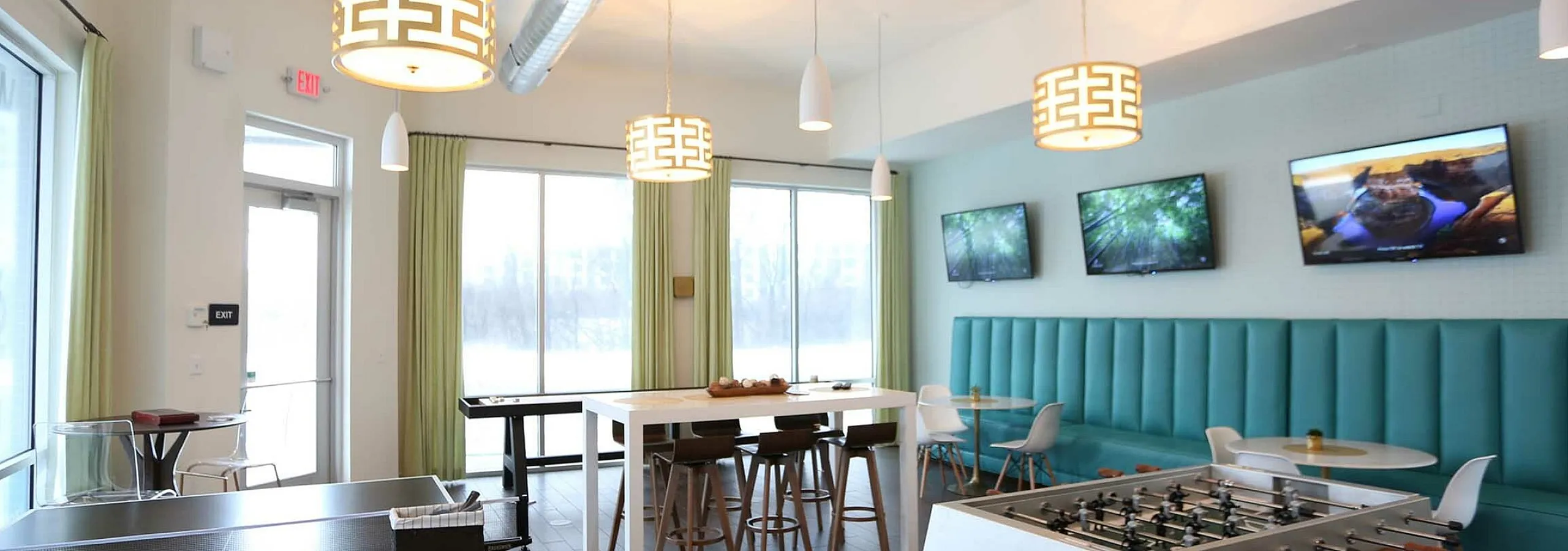 Modern communal space featuring stylish pendant lighting, multiple TVs, table games, and a cozy seating area with teal accents.