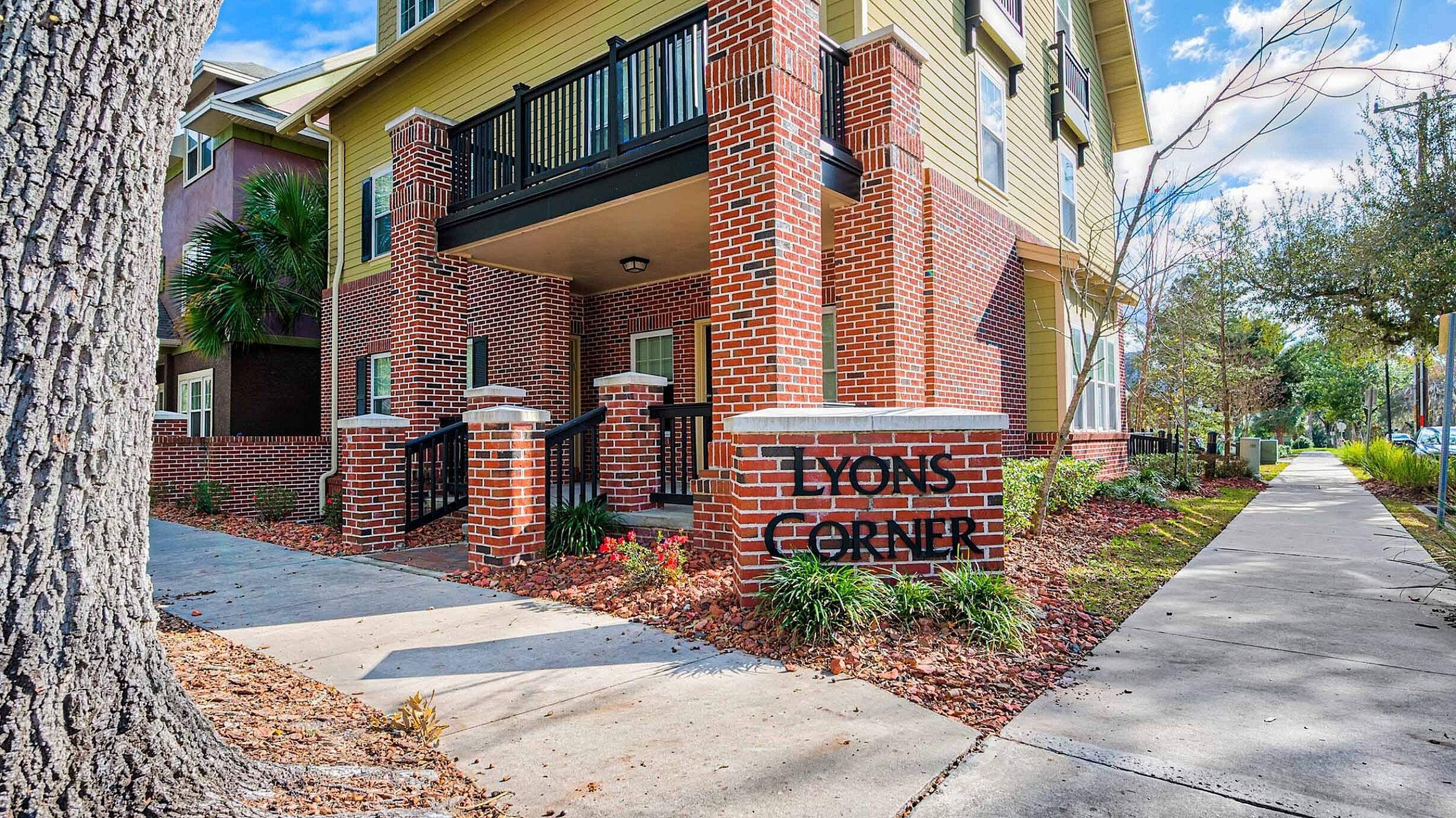 Charming brick facade of Lyon's Corner apartment complex, nestled in a serene tree-lined street with modern architectural details.