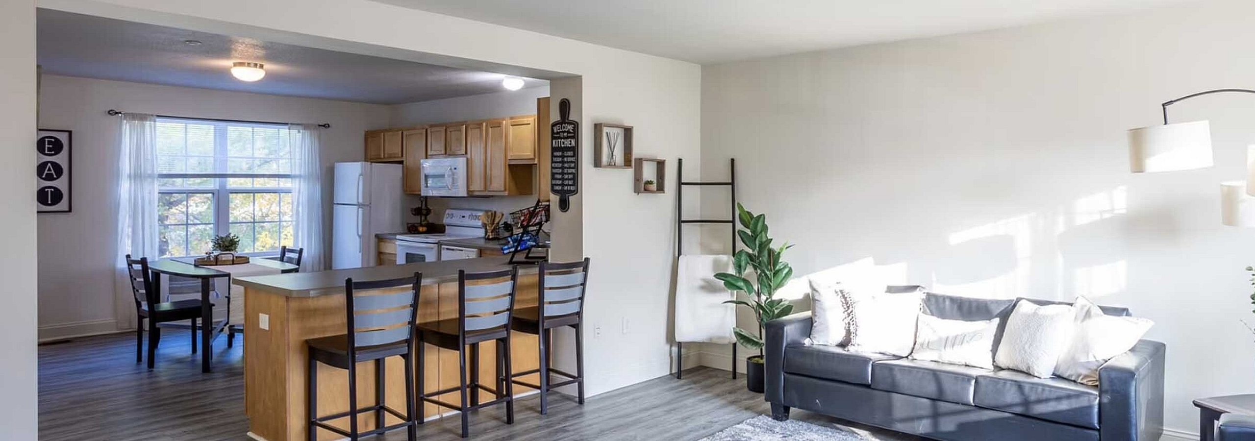 Bright and spacious open-concept living space featuring a modern kitchen with bar seating, a cozy living room, and large windows for natural light.