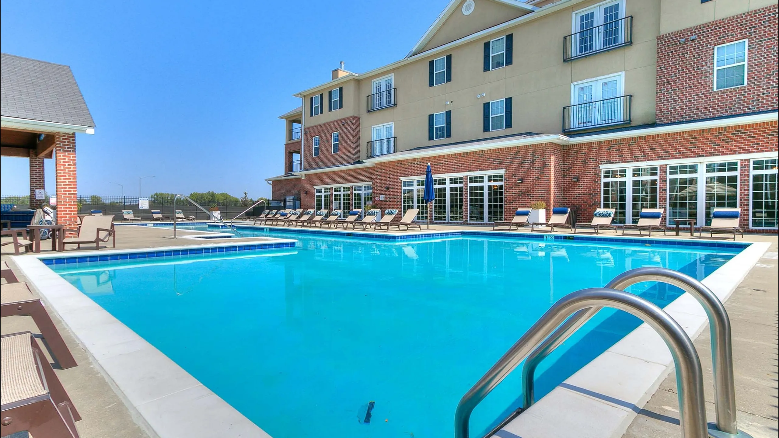 Luxurious apartment complex featuring a sparkling pool, comfortable loungers, and elegant architecture under a clear blue sky.