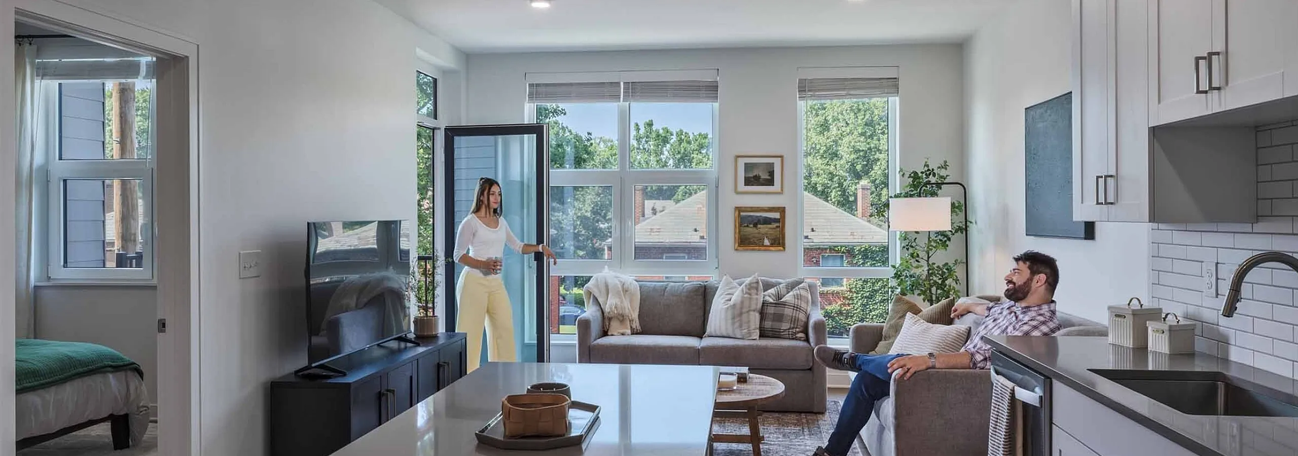 Bright, contemporary open-concept living area featuring a sleek kitchen and cozy lounge. Large windows reveal beautiful, lush green views.