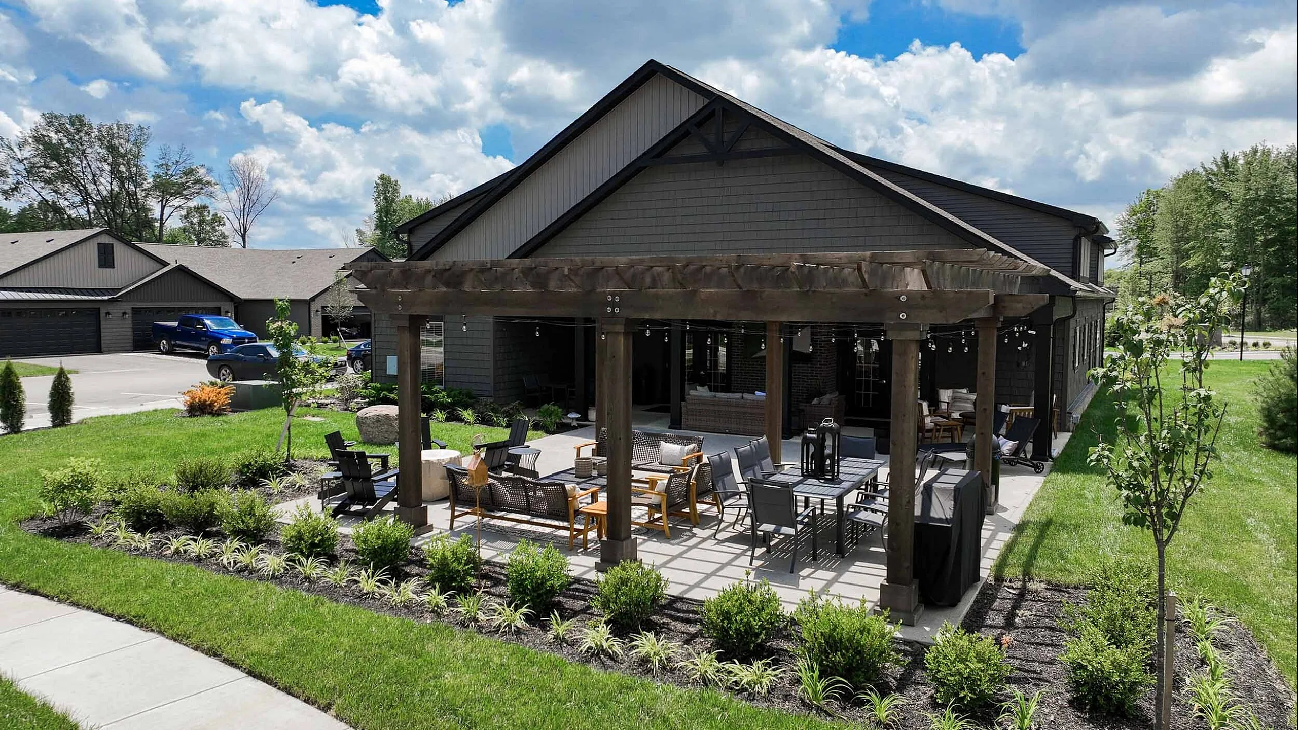 Charming outdoor patio with stylish pergola, perfect for entertaining, surrounded by lush greenery and set against a modern house with a spacious driveway.