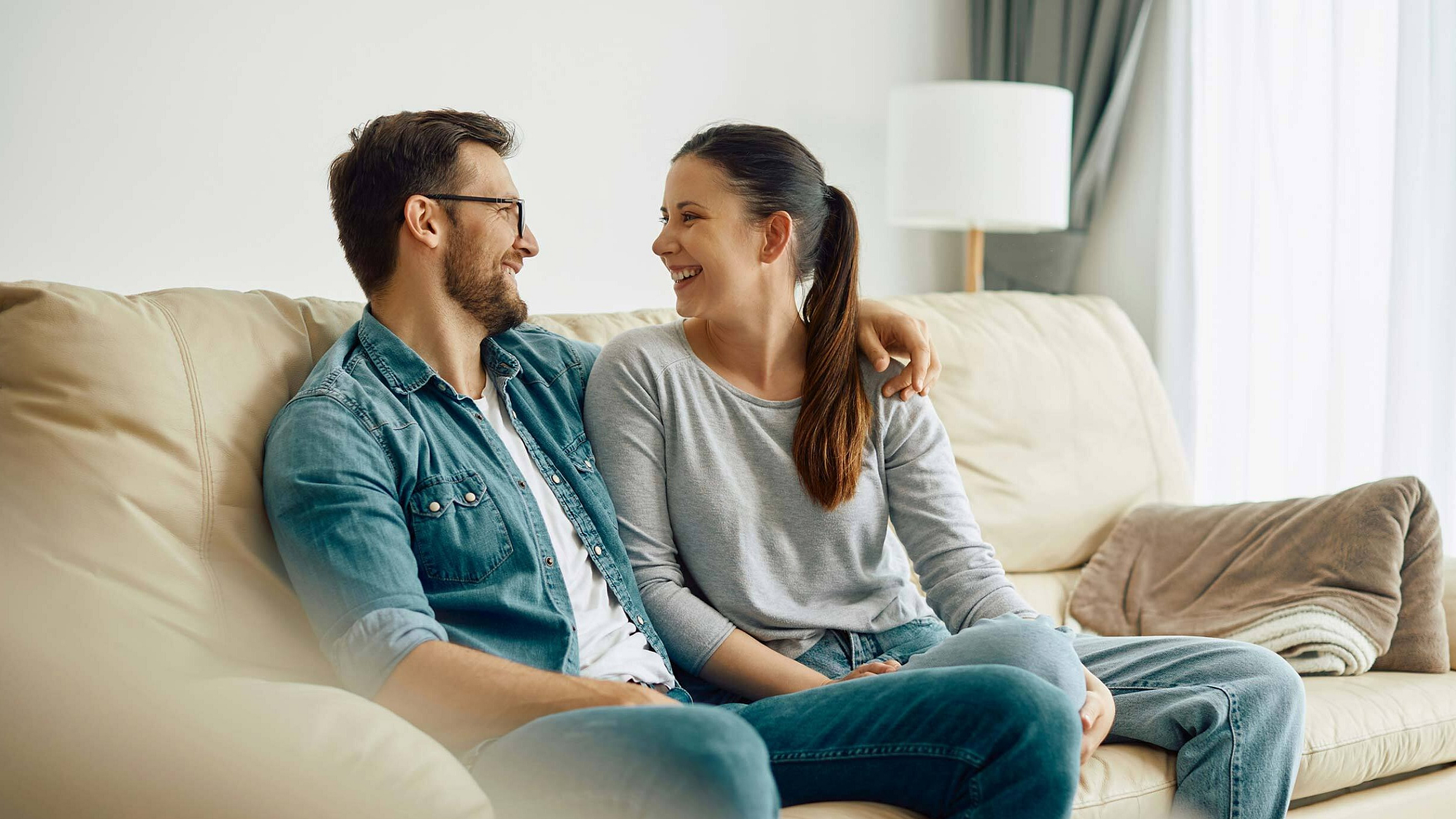 Cozy living room with a cheerful couple relaxing on a comfortable beige sofa, creating a warm and inviting atmosphere.
