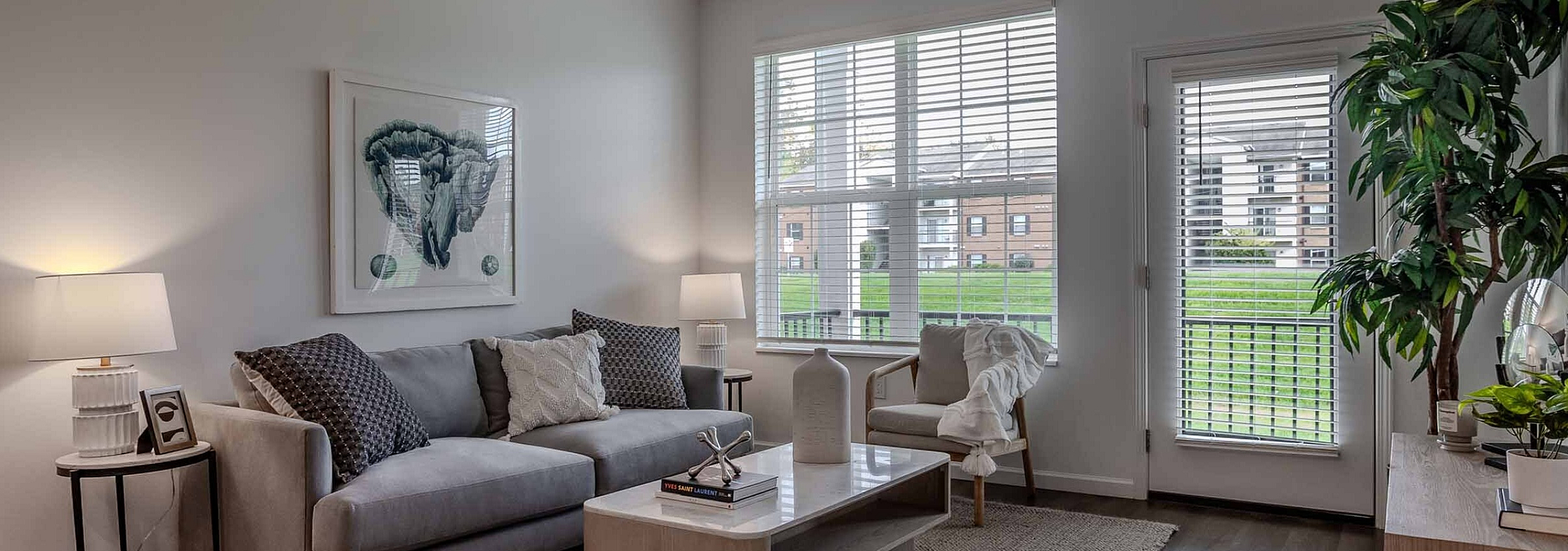Inviting living room with elegant decor, featuring a plush gray sofa, a chic coffee table, and large windows letting in natural light.