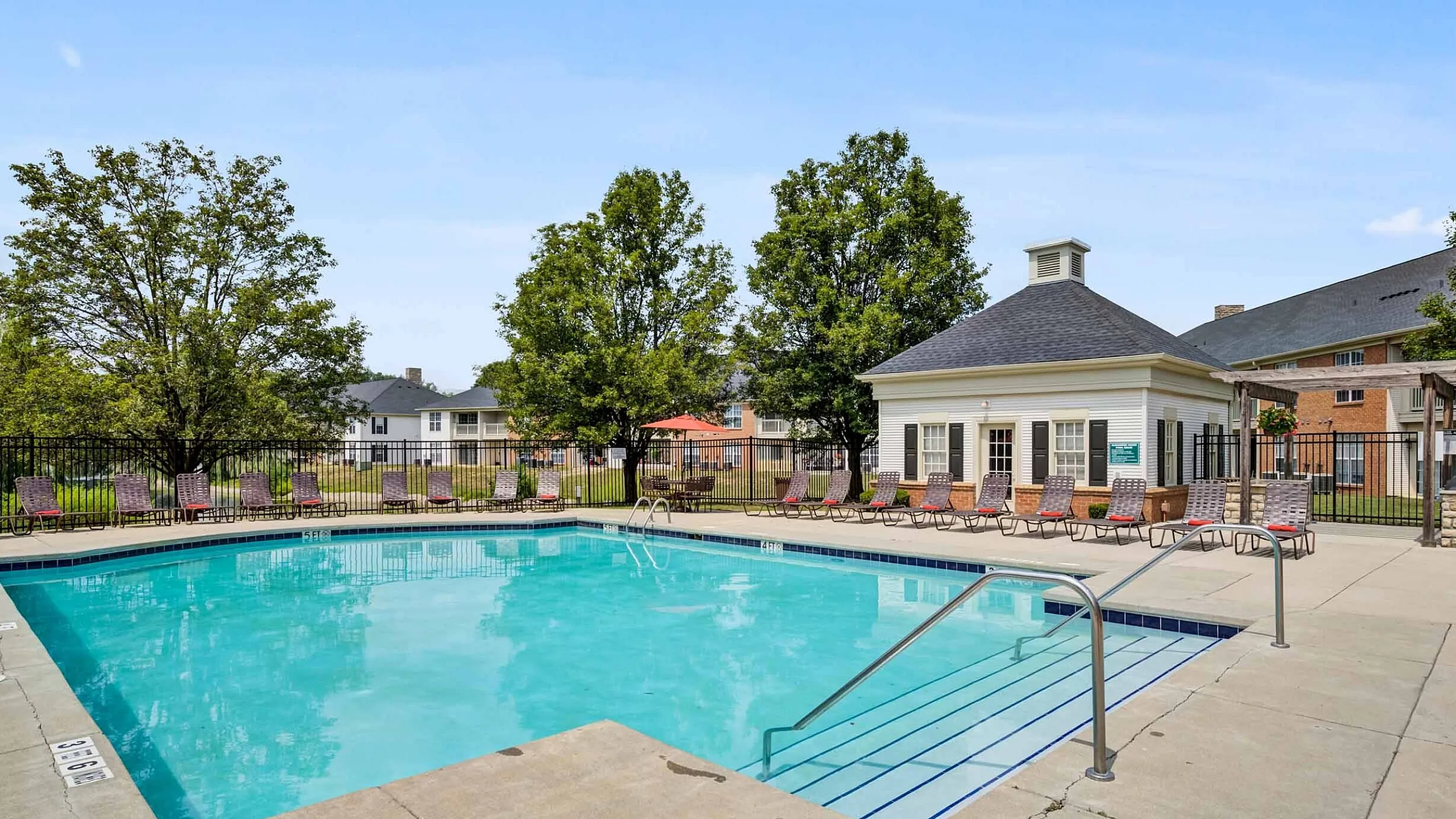 Inviting outdoor pool area with lounge chairs and charming clubhouse surrounded by lush greenery.