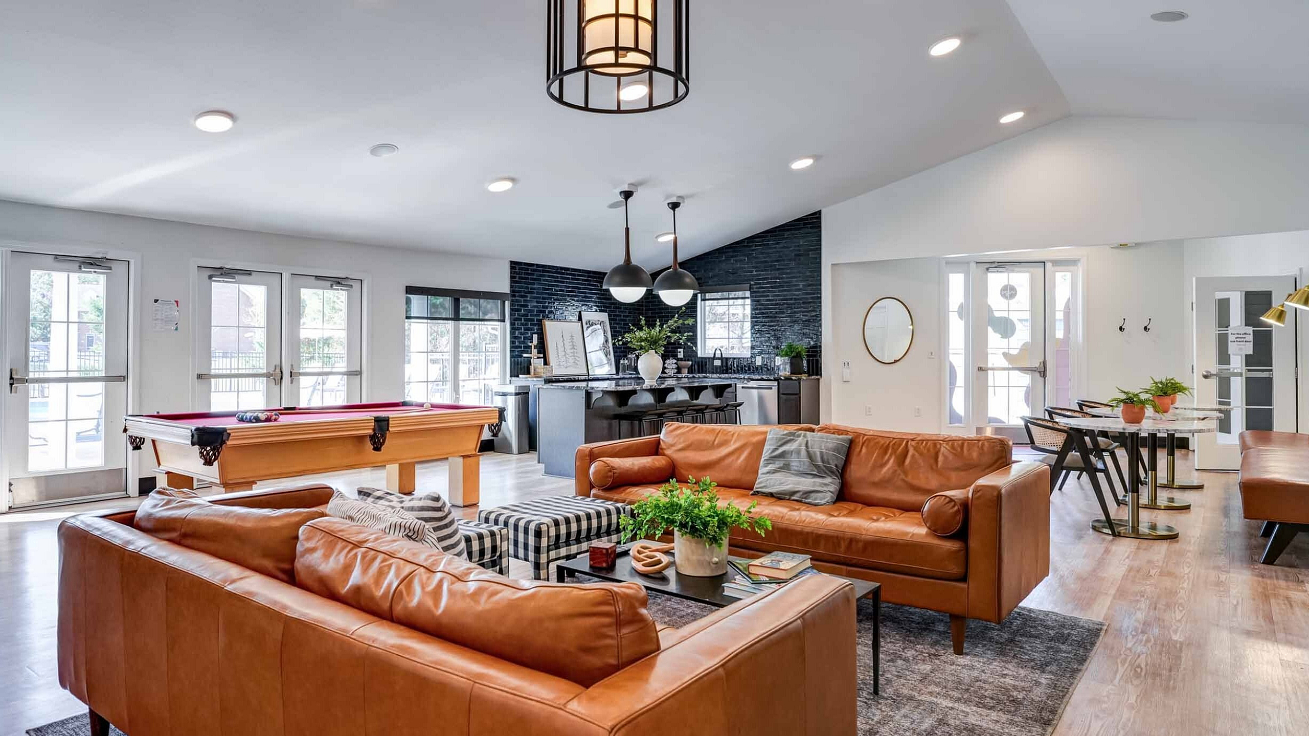 Modern and elegant living space featuring leather sofas, stylish pendant lights, a billiards table, and a chic open-concept kitchen.