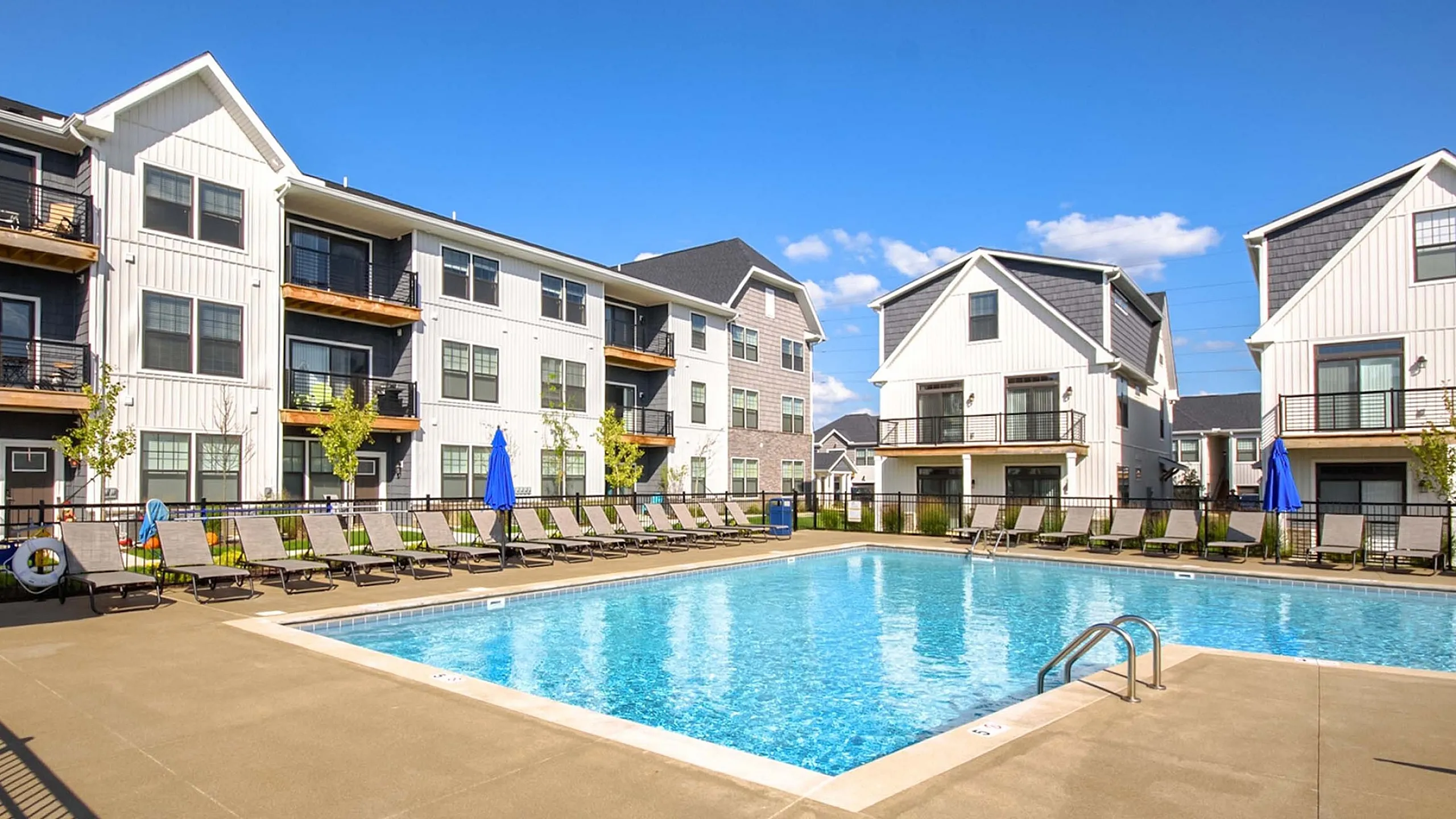 Charming residential complex featuring modern apartments with balconies, surrounding a sparkling swimming pool under a clear blue sky.