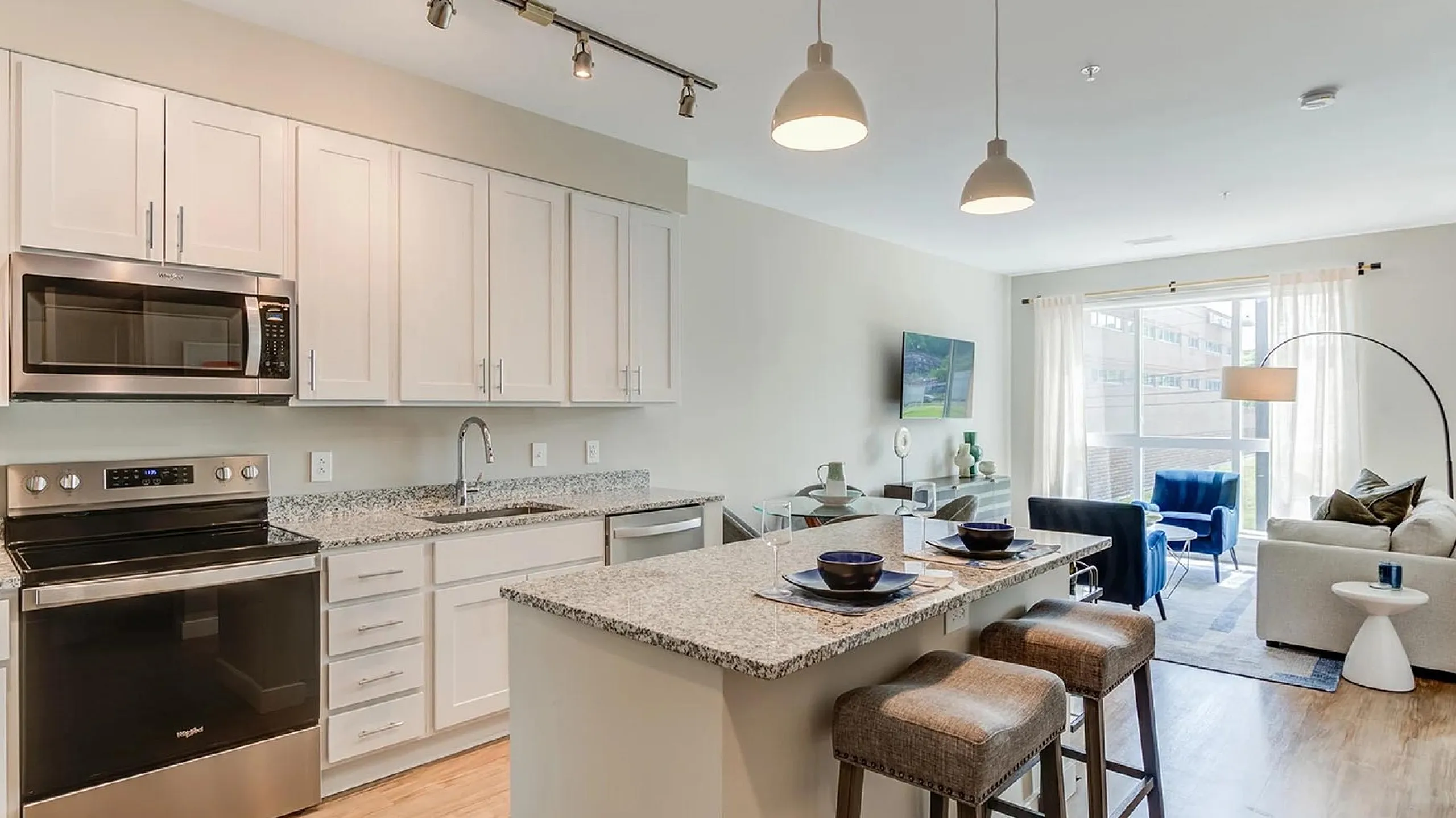 Modern open-concept kitchen and living room with granite countertops, sleek appliances, and bright natural lighting.