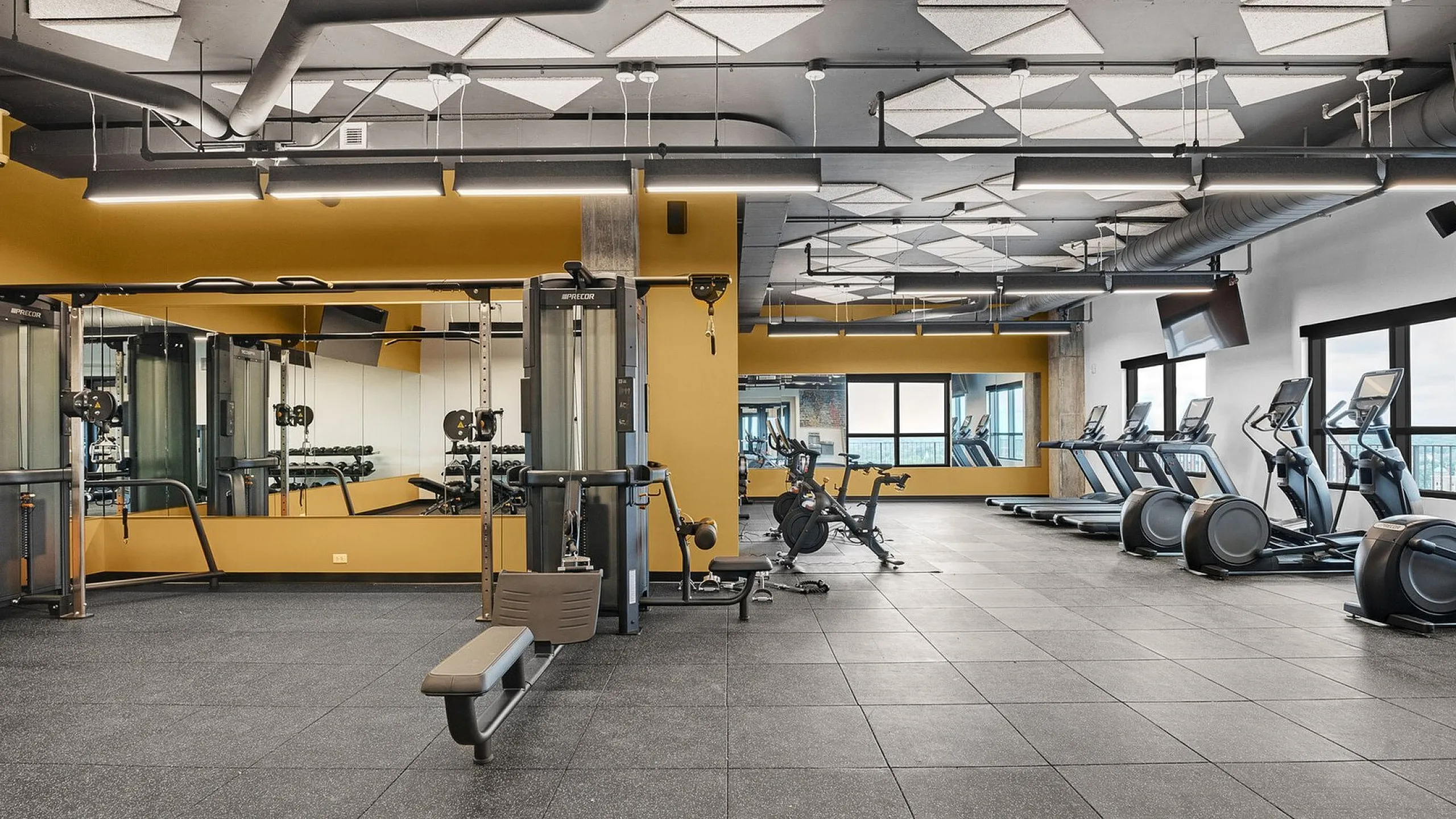 Modern, well-equipped fitness center featuring state-of-the-art exercise machines, large mirrors, and stylish geometric ceiling designs.