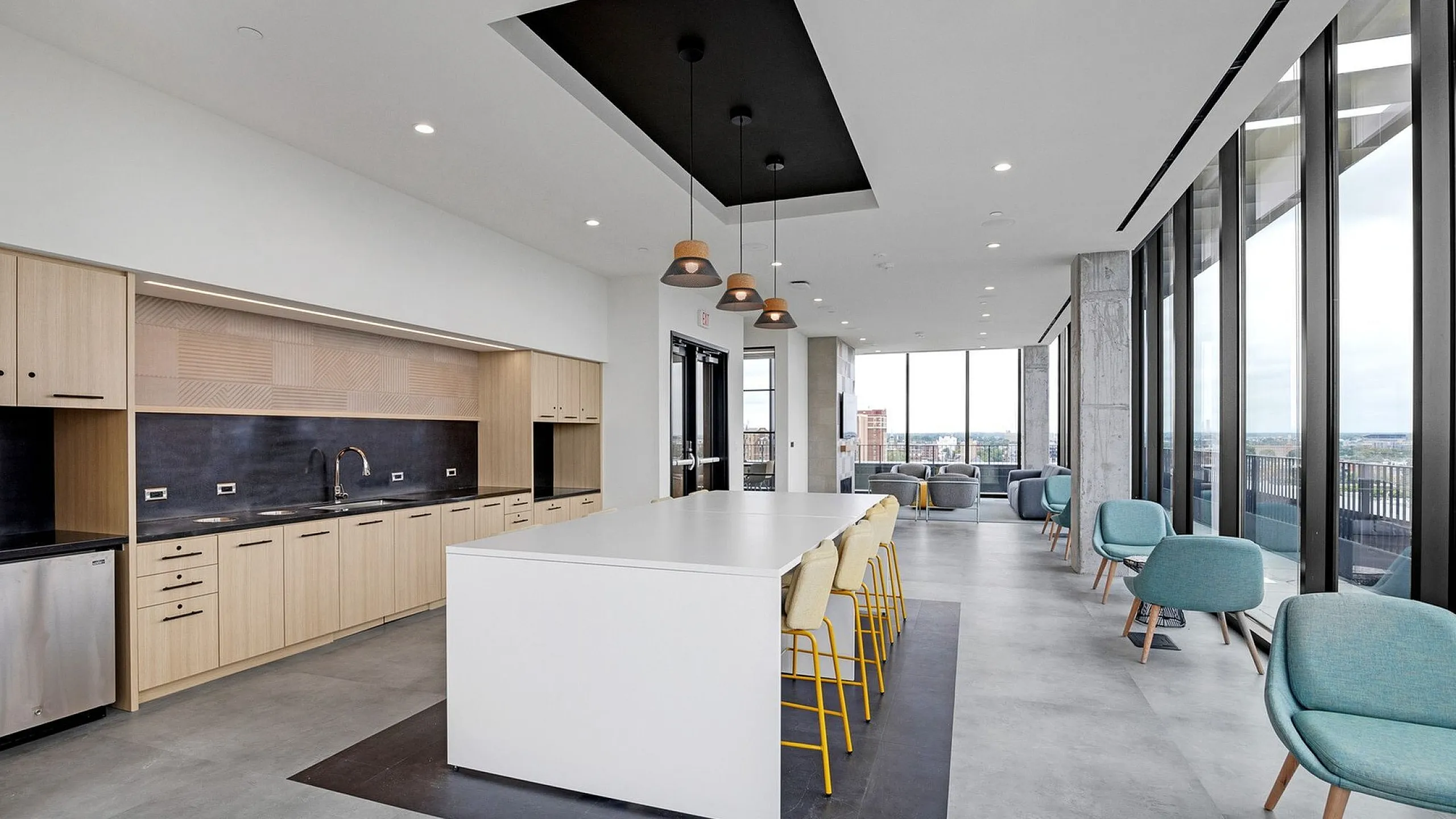 Elegant modern kitchen and lounge area with sleek cabinetry, a large island with seating, pendant lighting, and expansive windows offering stunning city views.