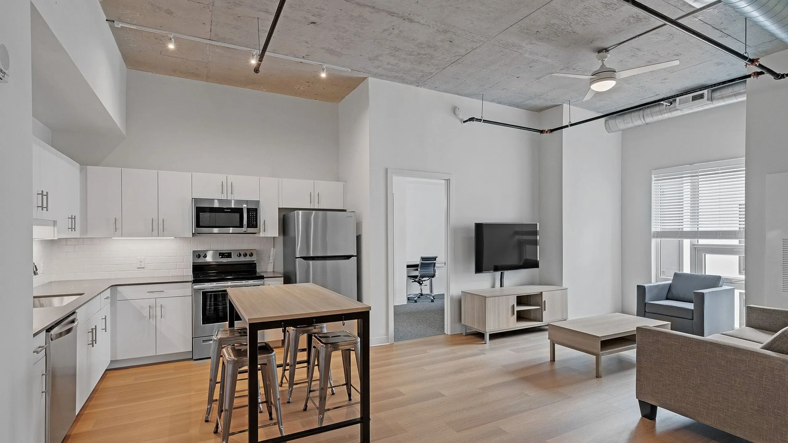 Modern open-plan apartment with sleek kitchen, stainless steel appliances, cozy living area, and industrial-style ceiling.