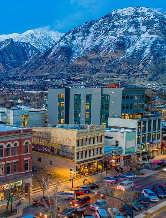 Stunning aerial view of a lively city with a historic brick building and snow-capped mountains in the background.