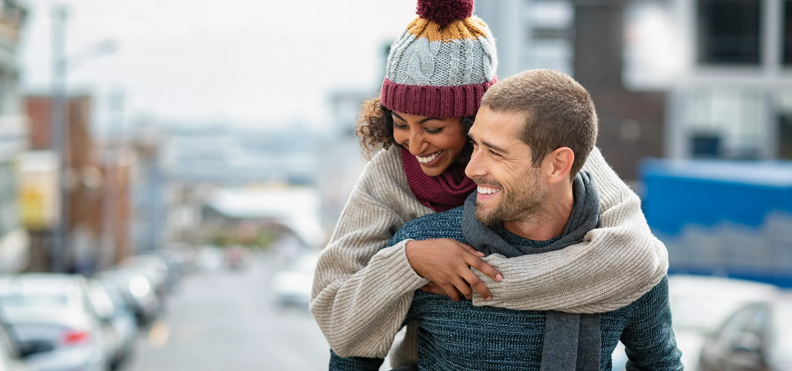 Smiling couple enjoying a playful piggyback ride on a city street.