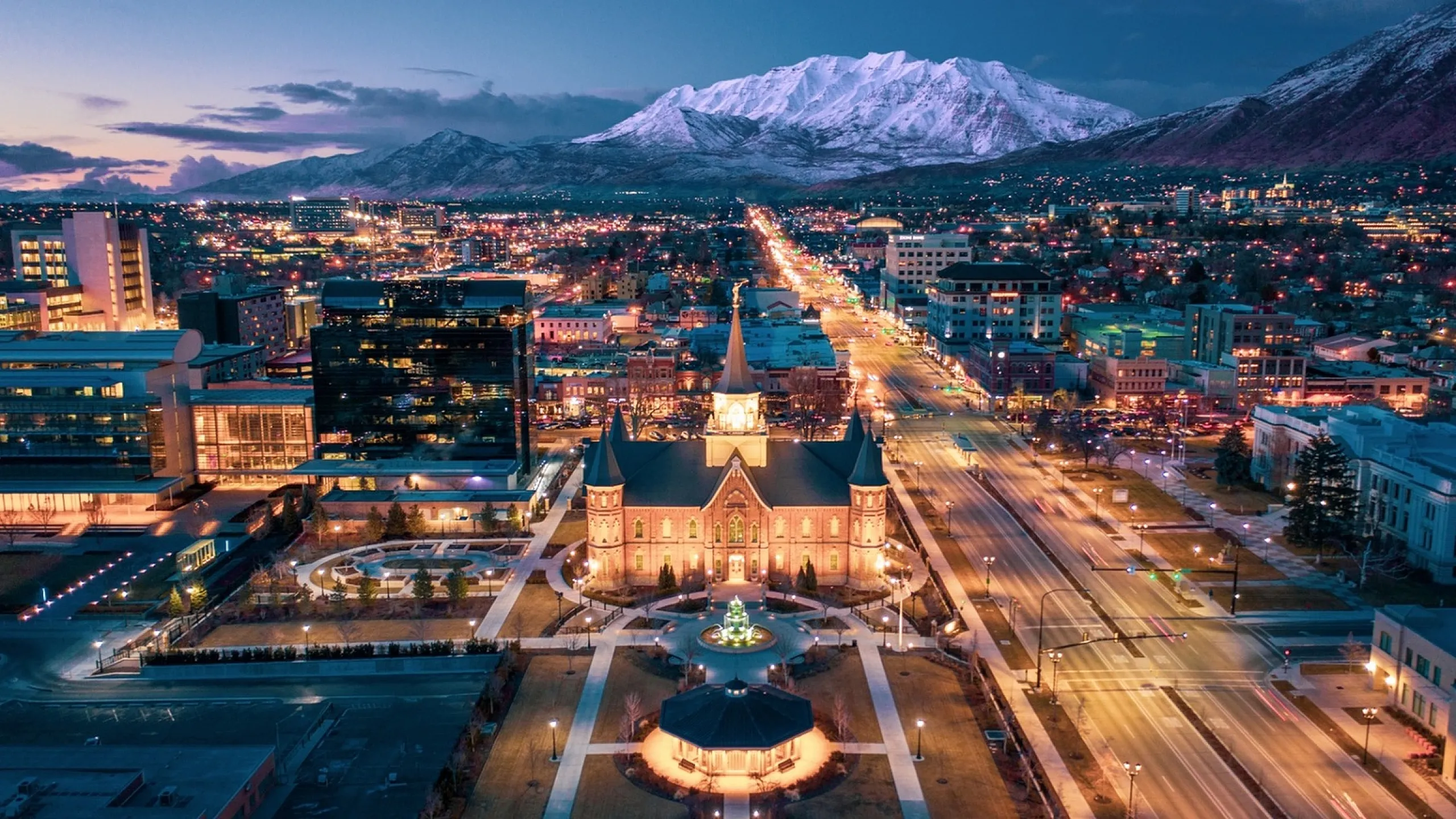 Breathtaking view of a city illuminated at dusk, with majestic mountains in the background.