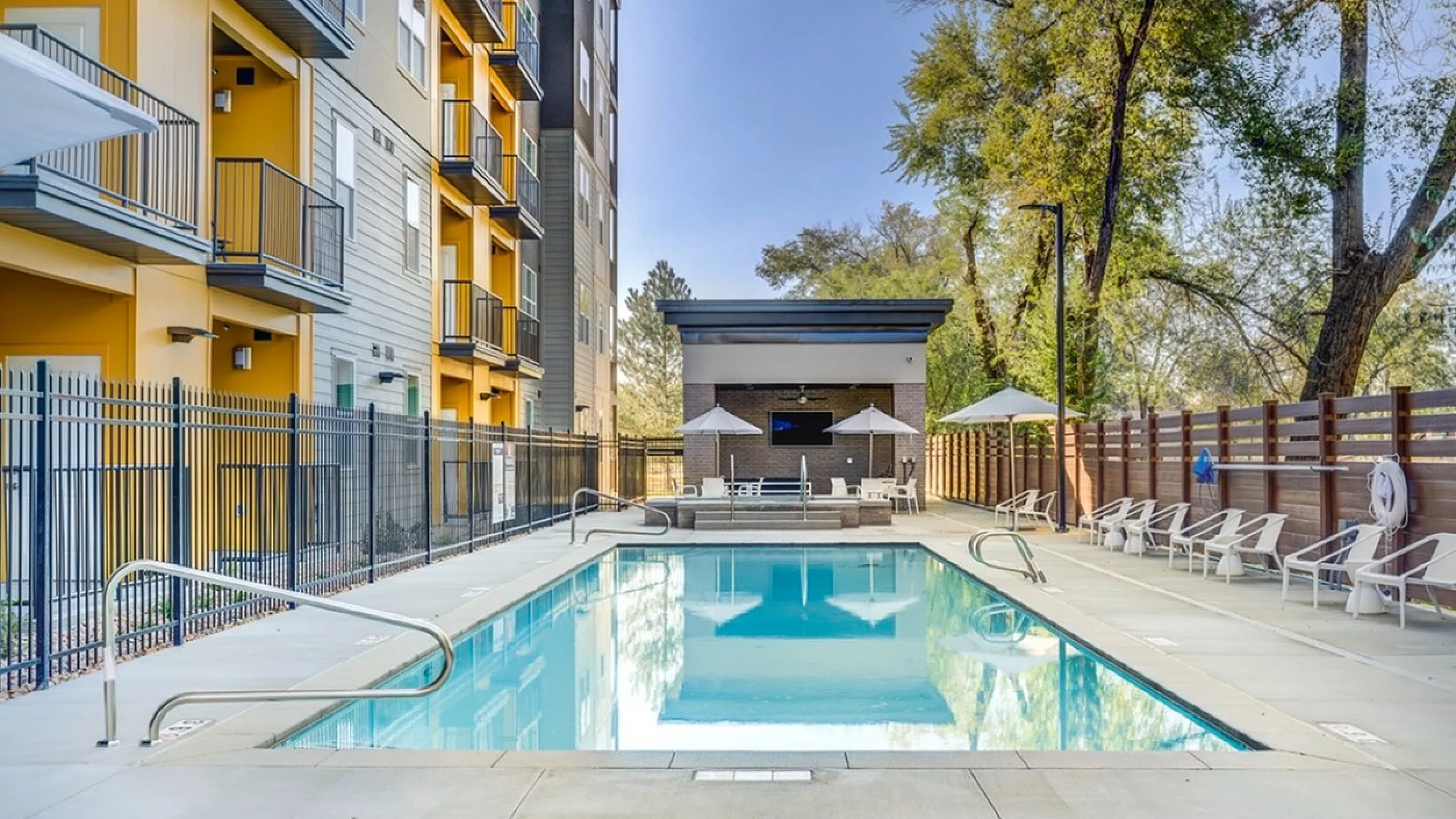 Inviting outdoor pool area with lounge chairs and shaded seating, surrounded by modern apartments and lush greenery.