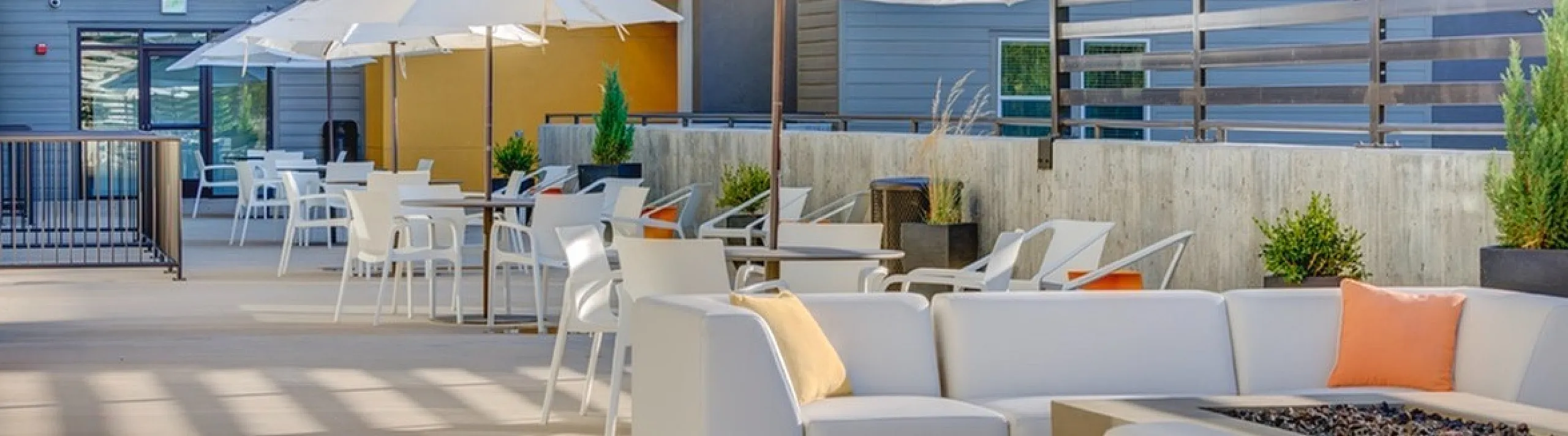Modern outdoor seating area with stylish white sofas and large umbrellas, perfect for relaxation and social gatherings in a chic apartment complex setting.