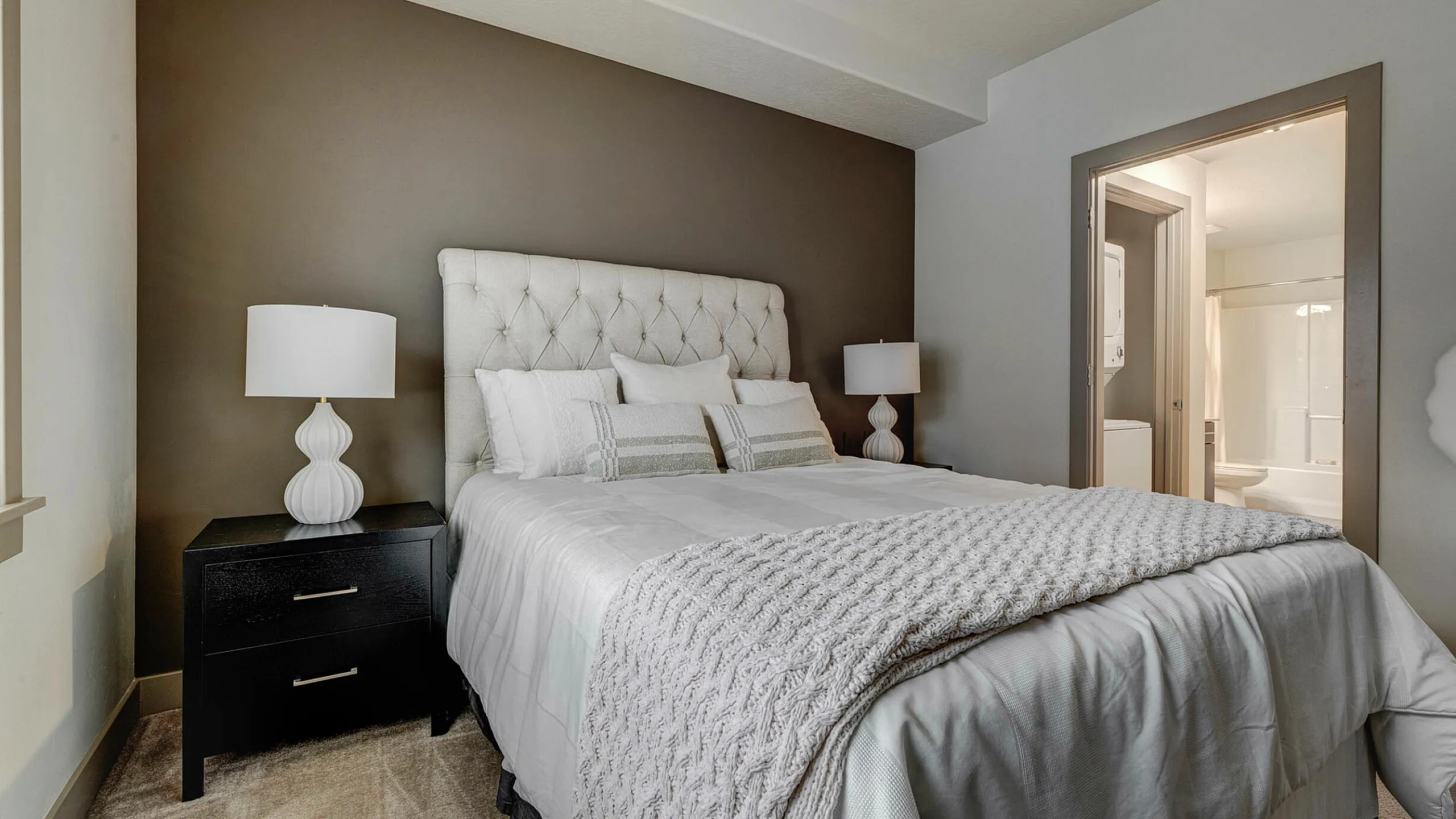 Inviting bedroom with a plush tufted headboard, elegant bedside lamps, and direct access to a modern en-suite bathroom.