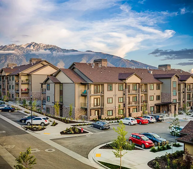 Scenic apartment complex nestled against stunning mountain backdrop, featuring modern architecture and ample parking.