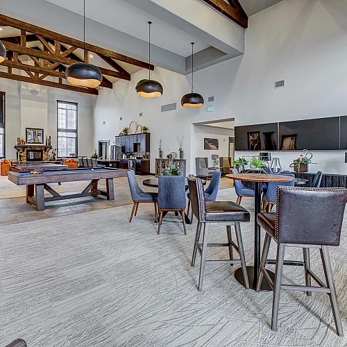 Elegant community lounge with high ceilings, modern lighting, and pool table, featuring cozy seating areas and natural wood accents.