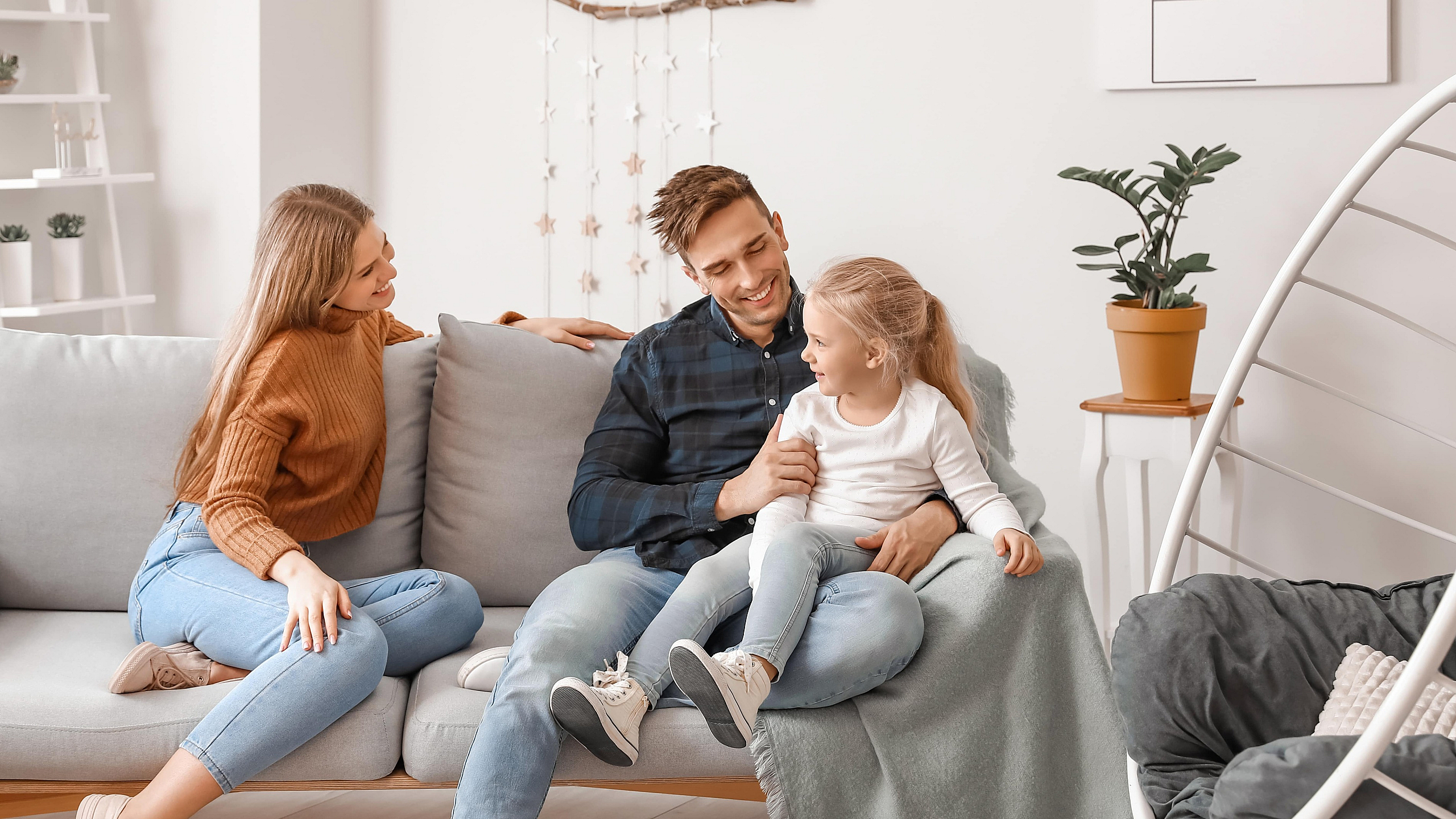 Cozy living room with a happy family seated on a modern gray sofa, surrounded by stylish decor and soft lighting.