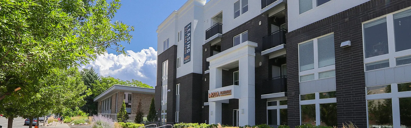 Modern apartment building with sleek design, lush landscaping, and bright facade under a clear blue sky.