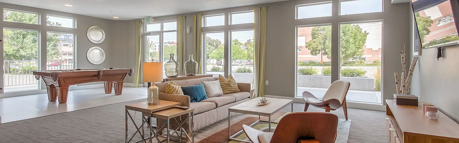 Spacious and bright modern living area featuring large windows, stylish furniture, and an elegant pool table, perfect for entertaining in a contemporary apartment.