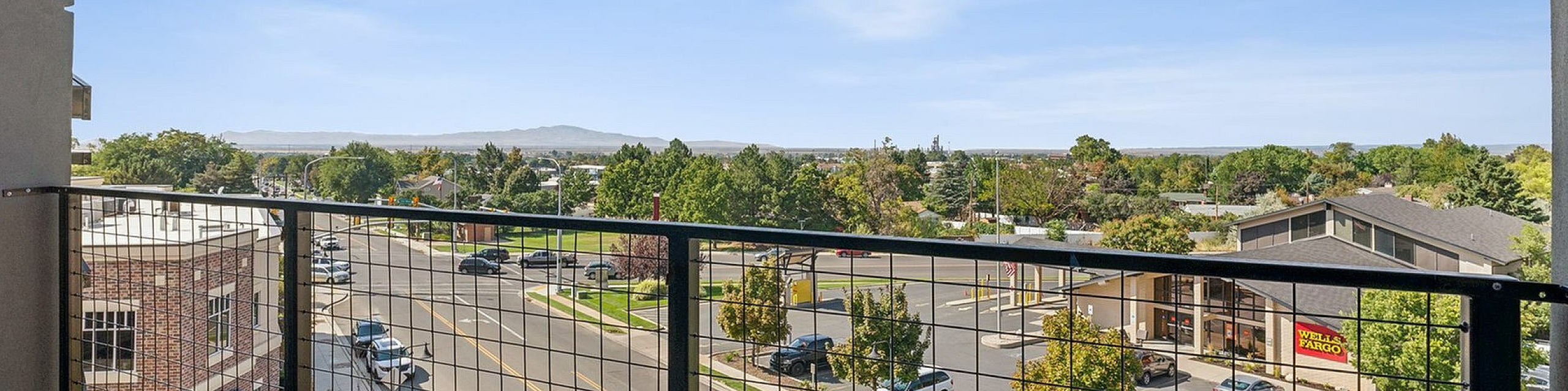 Charming balcony view overlooking a vibrant urban street with lush trees and a distant horizon.