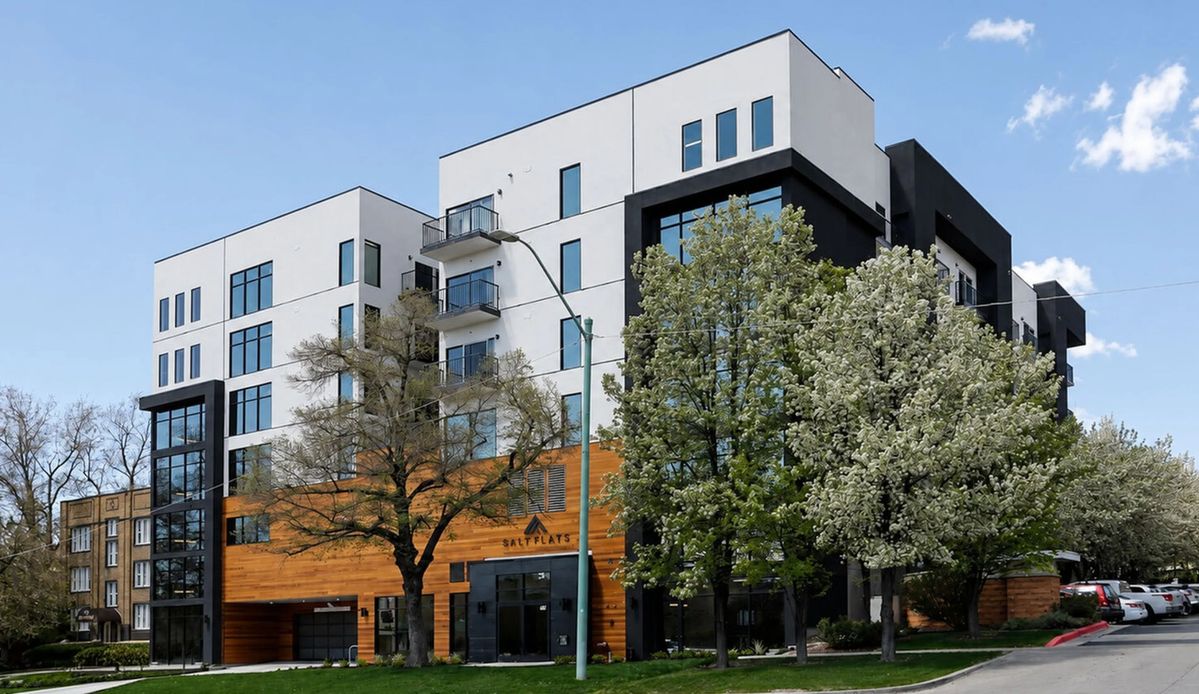 Modern apartment building with sleek white and black design, featuring expansive windows and surrounded by lush trees on a clear day.