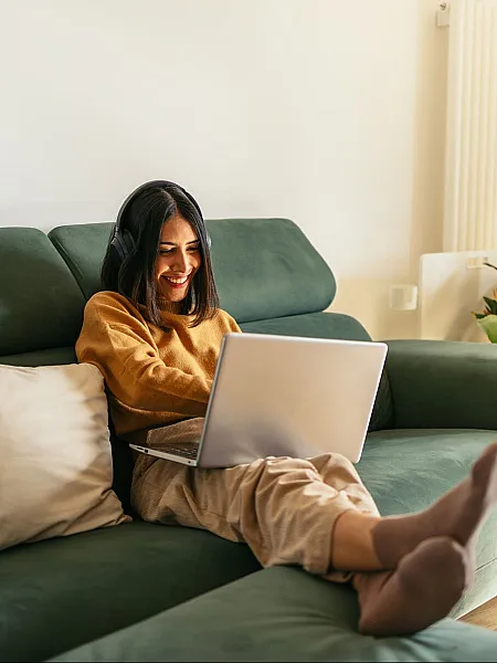 Cozy living space with a lush green sofa and a cheerful individual enjoying a laptop, perfect for relaxation and remote work.