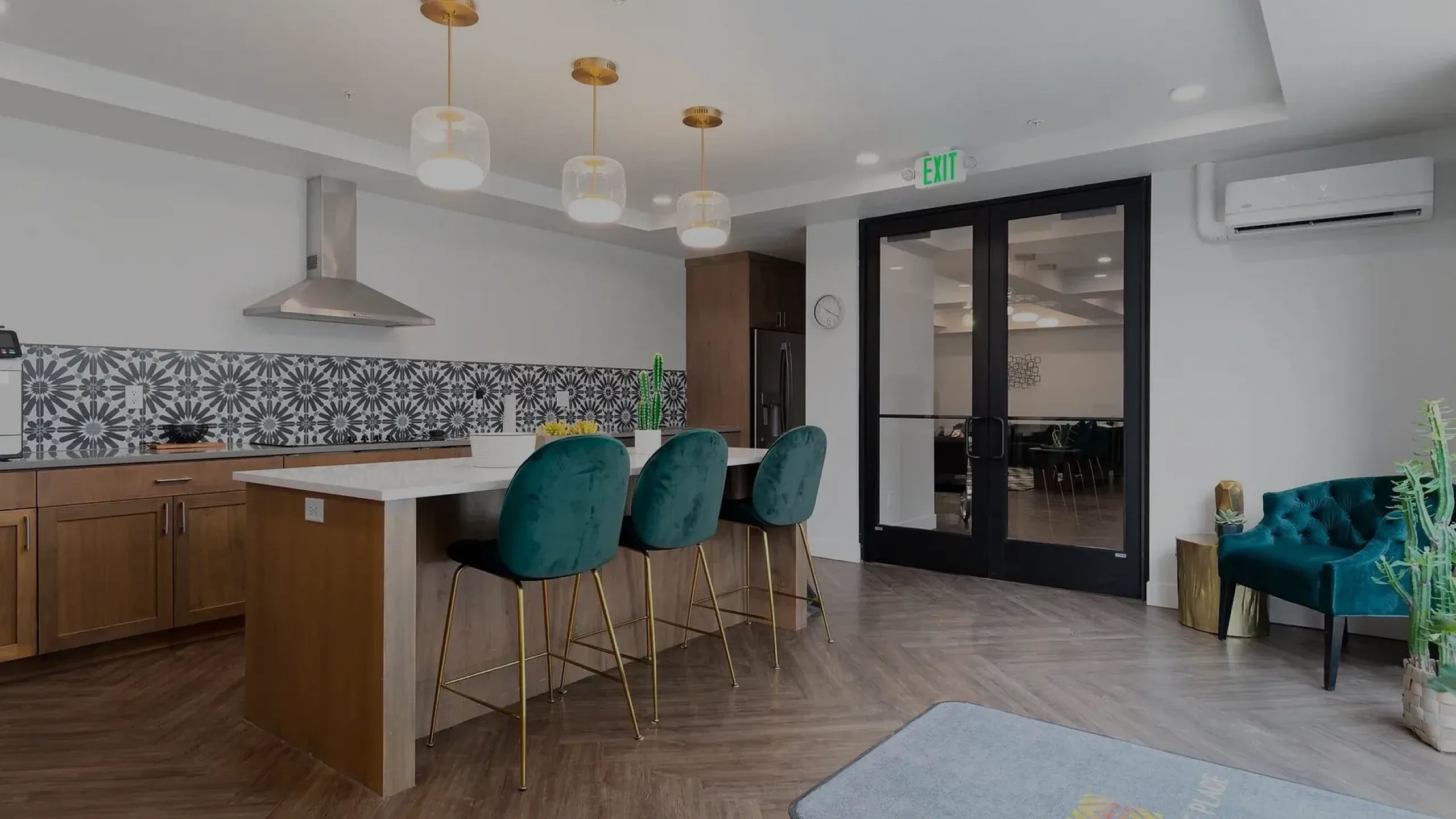 Contemporary kitchen interior with stylish patterned backsplash and modern pendant lighting above a chic island with green velvet barstools.