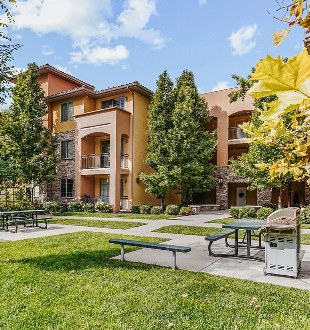 Charming apartment complex nestled amidst lush greenery, featuring modern architecture with spacious balconies, picnic area, and outdoor grill for relaxing gatherings.