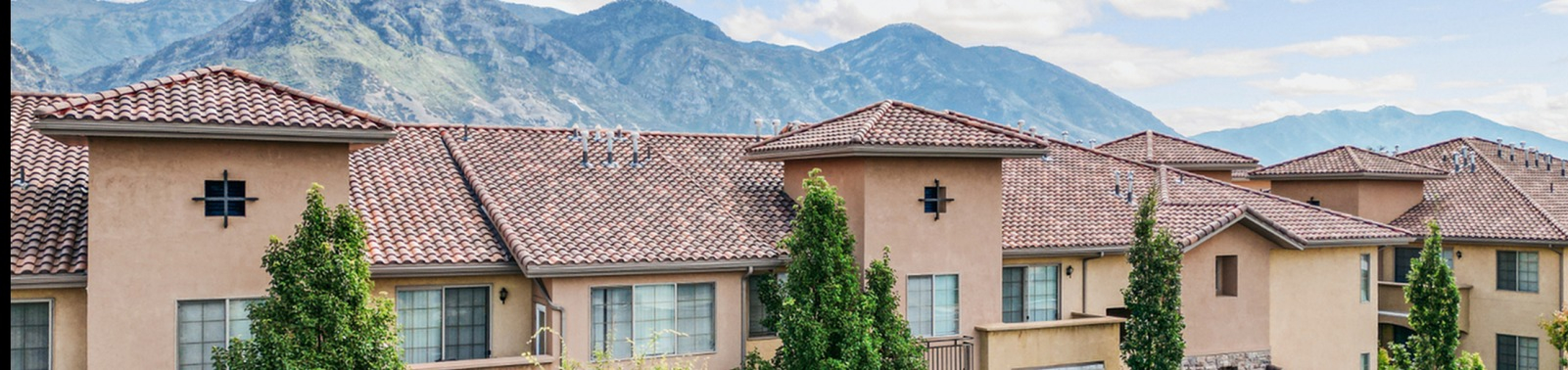 Charming Mediterranean-style apartment complex with red tile roofs and lush greenery, set against a backdrop of majestic mountains.