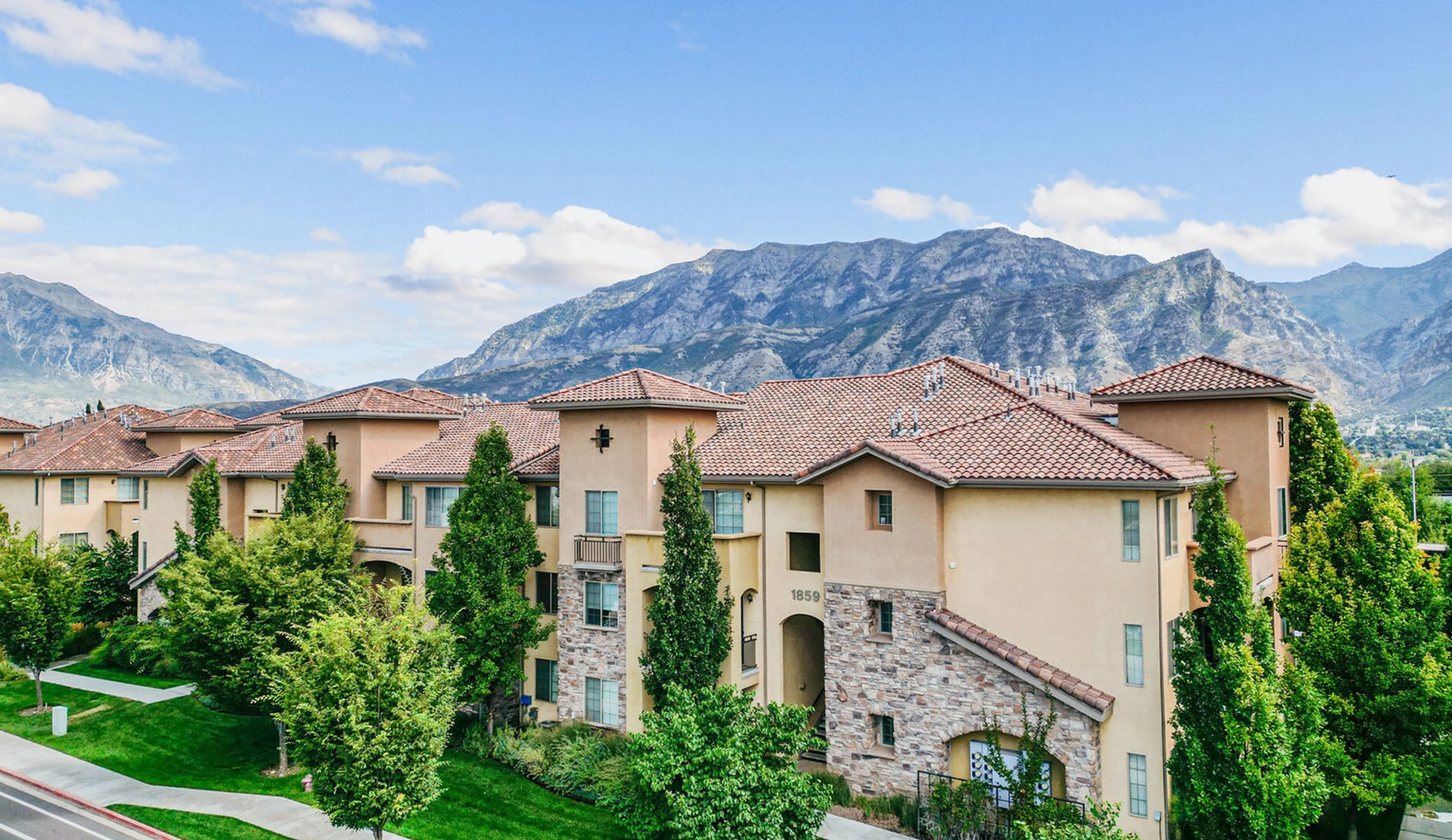 Charming apartment complex with stunning mountain backdrop, featuring Mediterranean-style architecture and lush greenery.