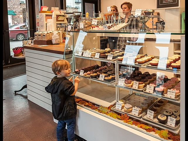 Cozy bakery with a charming display of colorful cupcakes and desserts, delighting a young child. Inviting ambiance with friendly staff in the background.