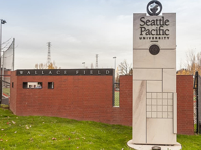 Entrance to Seattle Pacific University marked by a modern stone monument and brick wall, featuring the name 'Wallace Field', set against a lush green lawn.