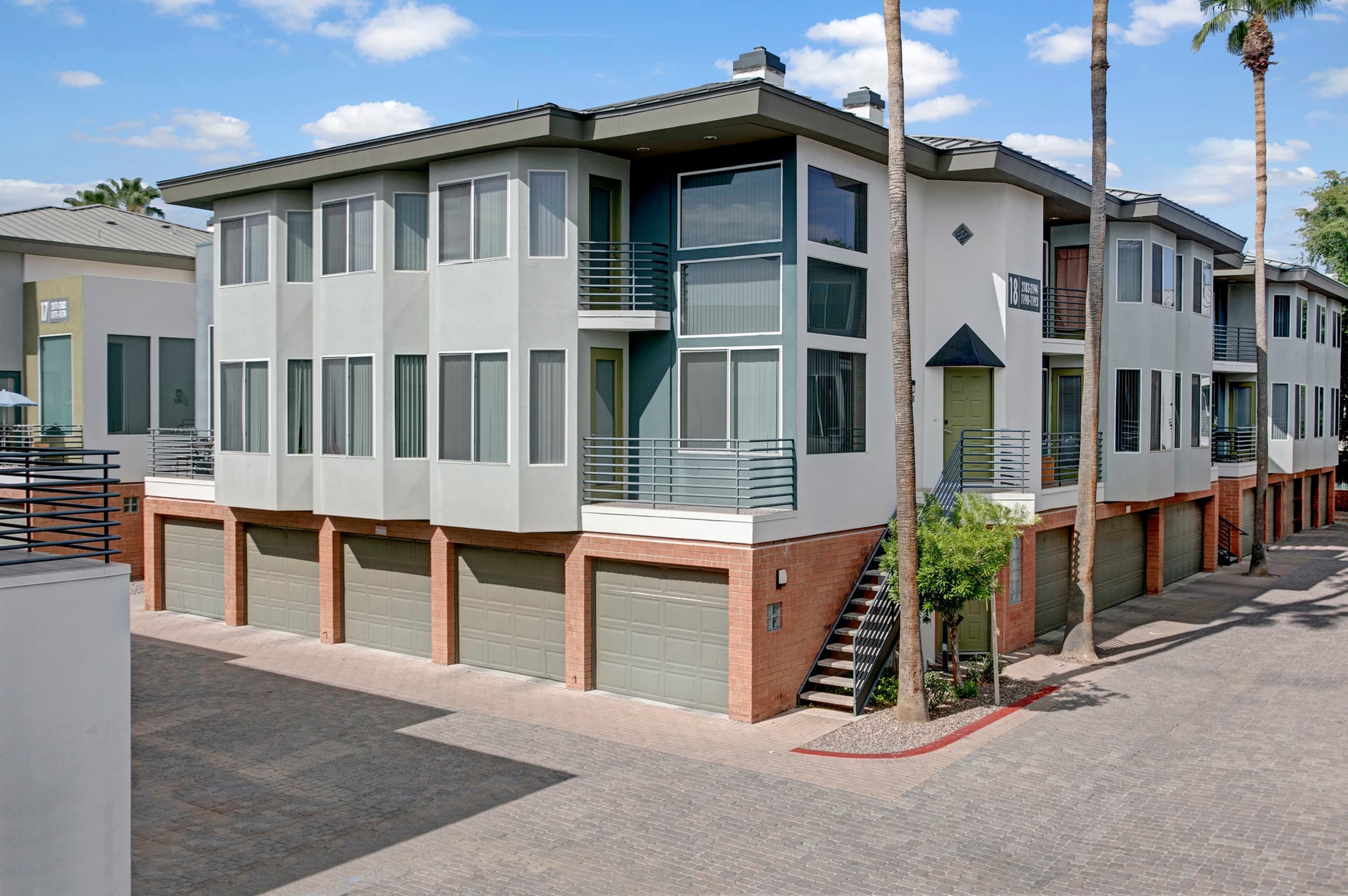 Contemporary multi-story apartment building with sleek design, large windows, and spacious garages under beautiful blue skies.