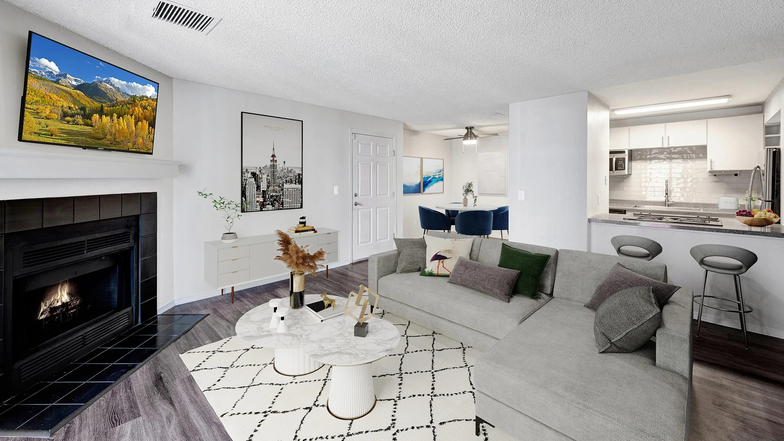 Bright and modern living room with gray sectional sofa, fireplace, TV, and open kitchen design.