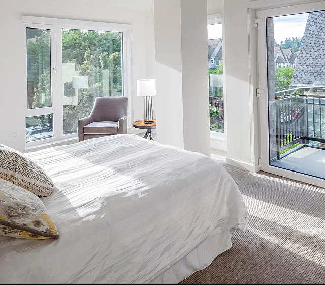 Elegant bedroom with large windows, a cozy bed, and a comfortable chair basking in natural sunlight.