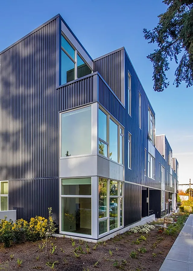 Modern apartment complex with sleek design and large windows, surrounded by vibrant landscaping and a clear blue sky.