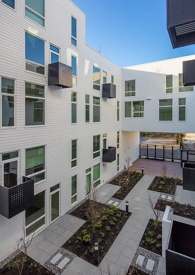 Modern apartment complex with sleek white facade and geometrical black balconies overlooking a landscaped courtyard.