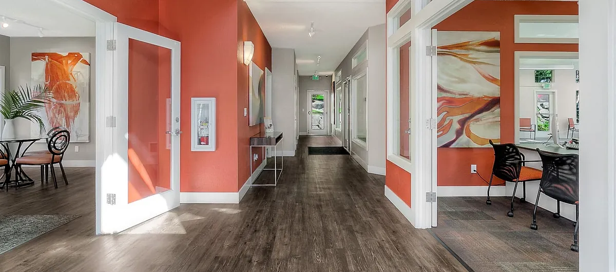 Vibrant open-space apartment hallway featuring modern decor, large windows, and stylish orange accent walls.