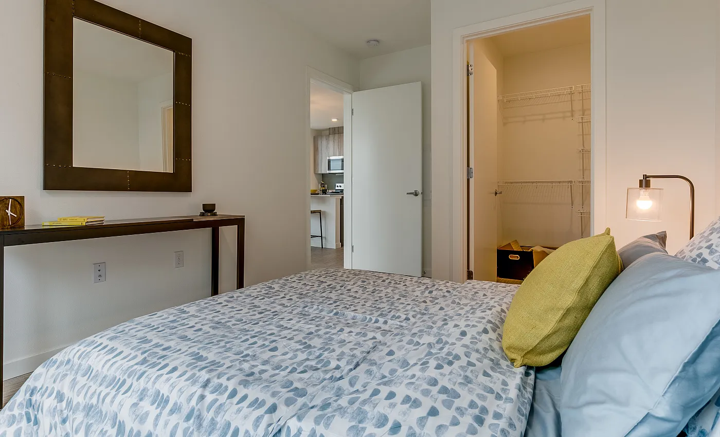 Modern and cozy bedroom with soft lighting, featuring a stylish bed, a large decorative mirror, and a spacious open closet.
