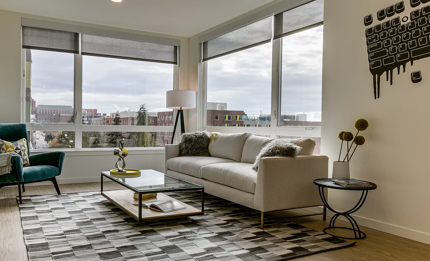 Modern living room with panoramic windows offering city views, elegant decor with a cozy sofa, stylish armchair, and contemporary art on the walls.
