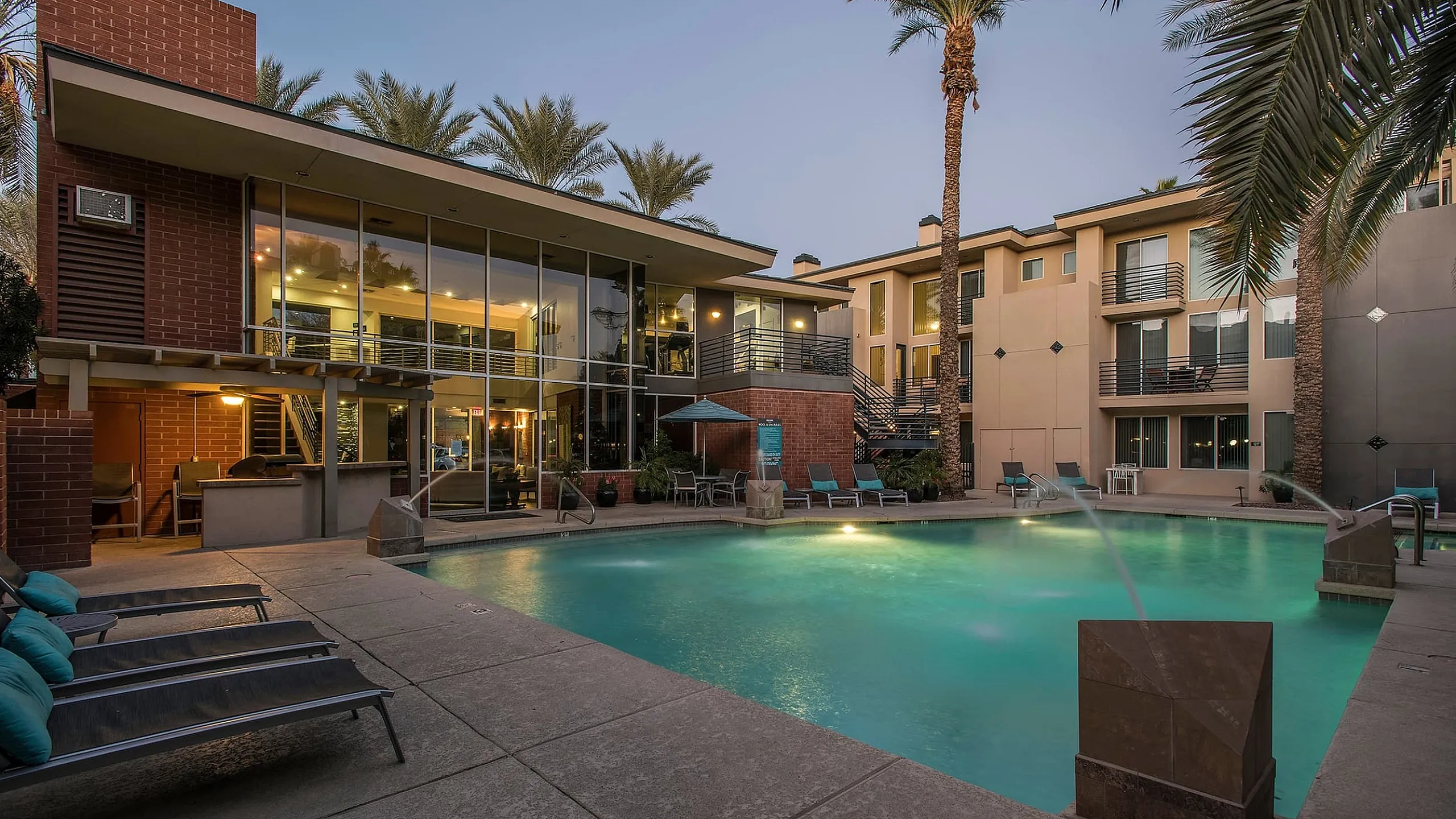 Modern apartment complex with large glass windows overlooking a luxurious pool surrounded by palm trees, creating a serene oasis for relaxation.