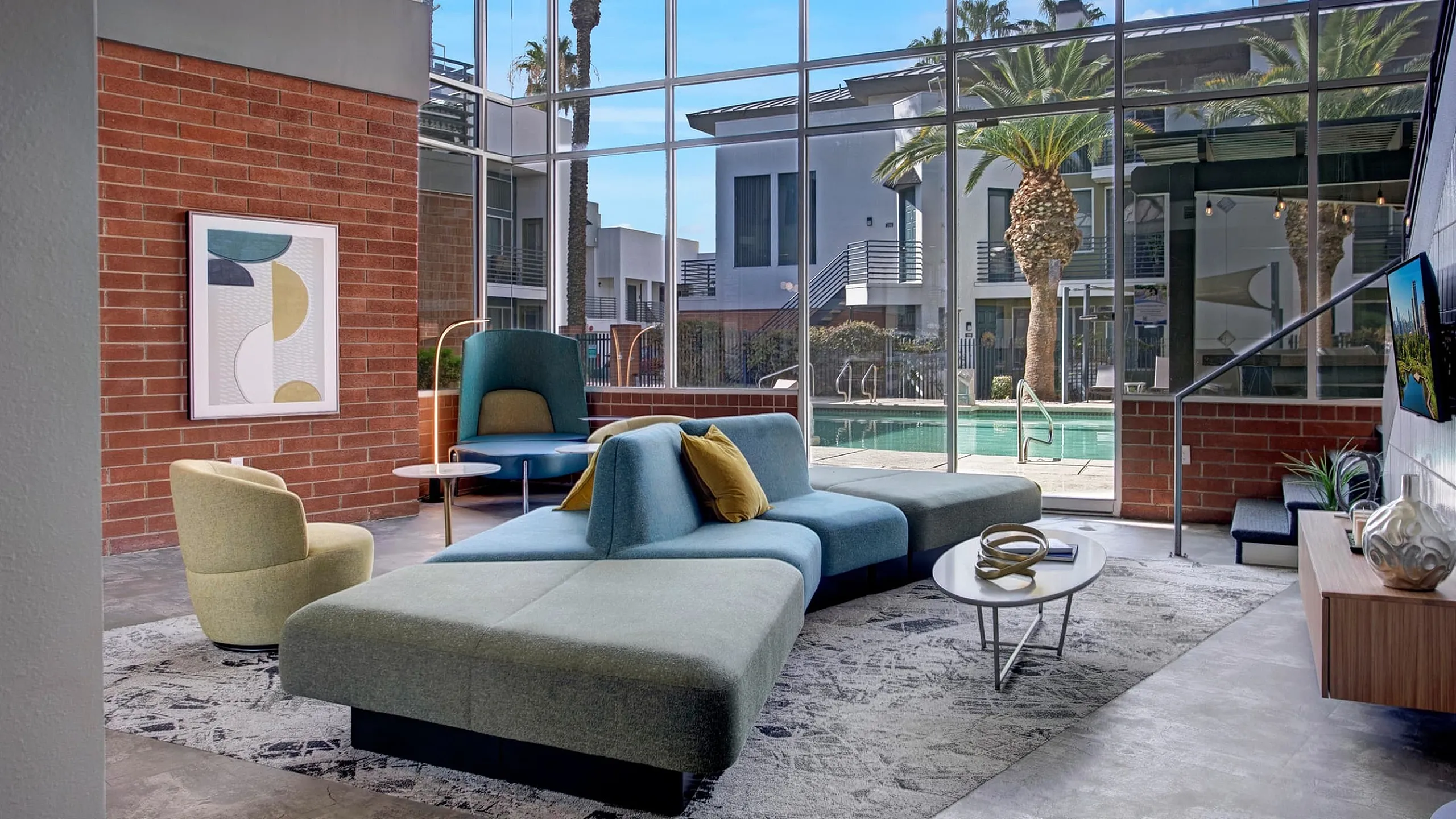 Modern living room with floor-to-ceiling windows, stylish seating, and a stunning view of the pool and palm trees.